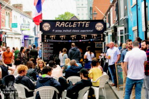 Raclette stall surrounded by people enjoying the sun at orange pip market