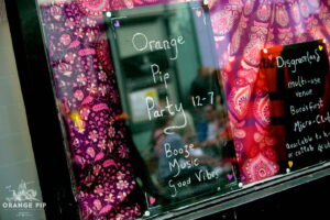 A sign in a window saying "Orange Pip Party 12-7, booze, music, good vibes"