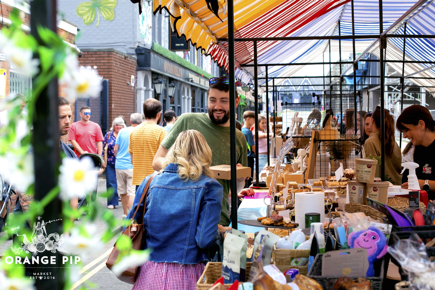 Two people chatting at a busy trade stall at a bustling Orange Pip market on Bedford Street