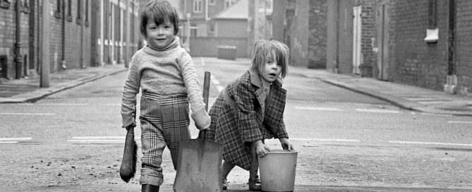 Two children carrying a bucket and a sweeping brush on a street in Teesside.